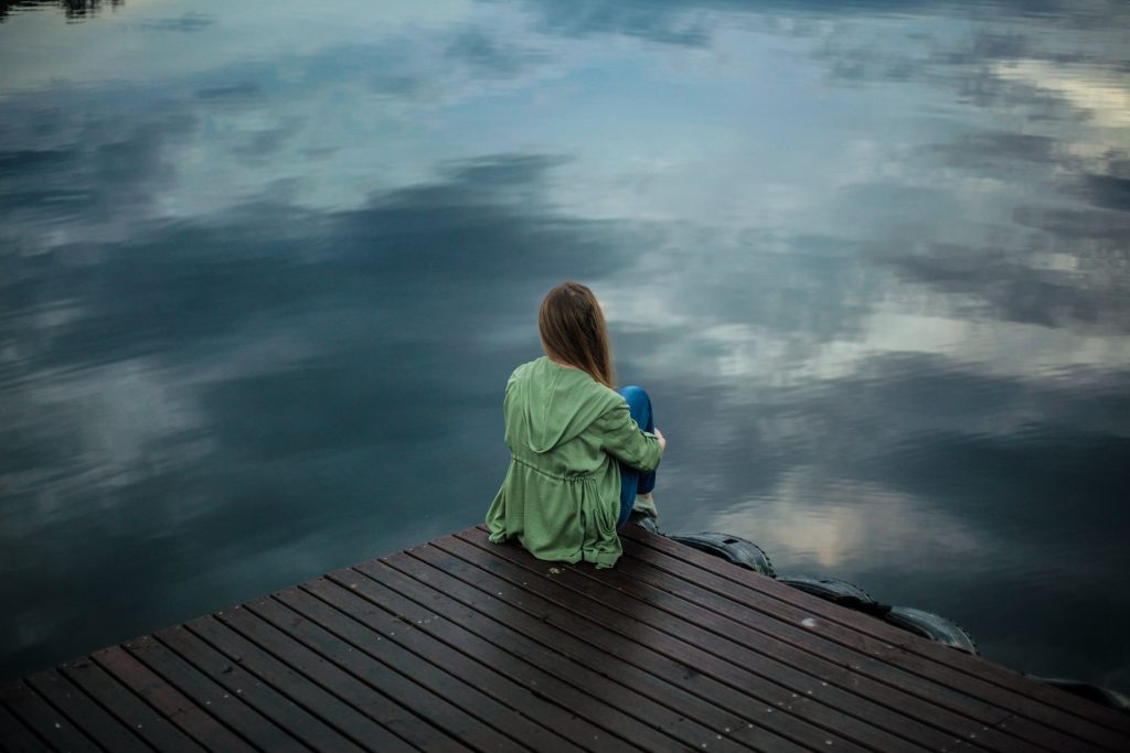 Woman sitting alone at the end of a dock on a cloudy day. Ways to overcome loneliness.