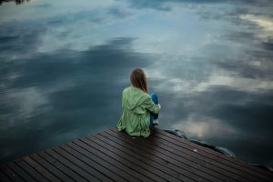 Woman sitting alone at the end of a dock on a cloudy day. Ways to overcome loneliness.