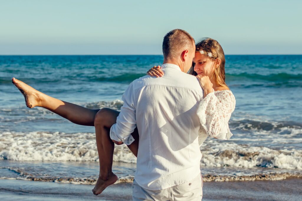 Man holding a woman up in his arms at a beach in a romantic way. Rekindling Passion, Romance, and Desire.