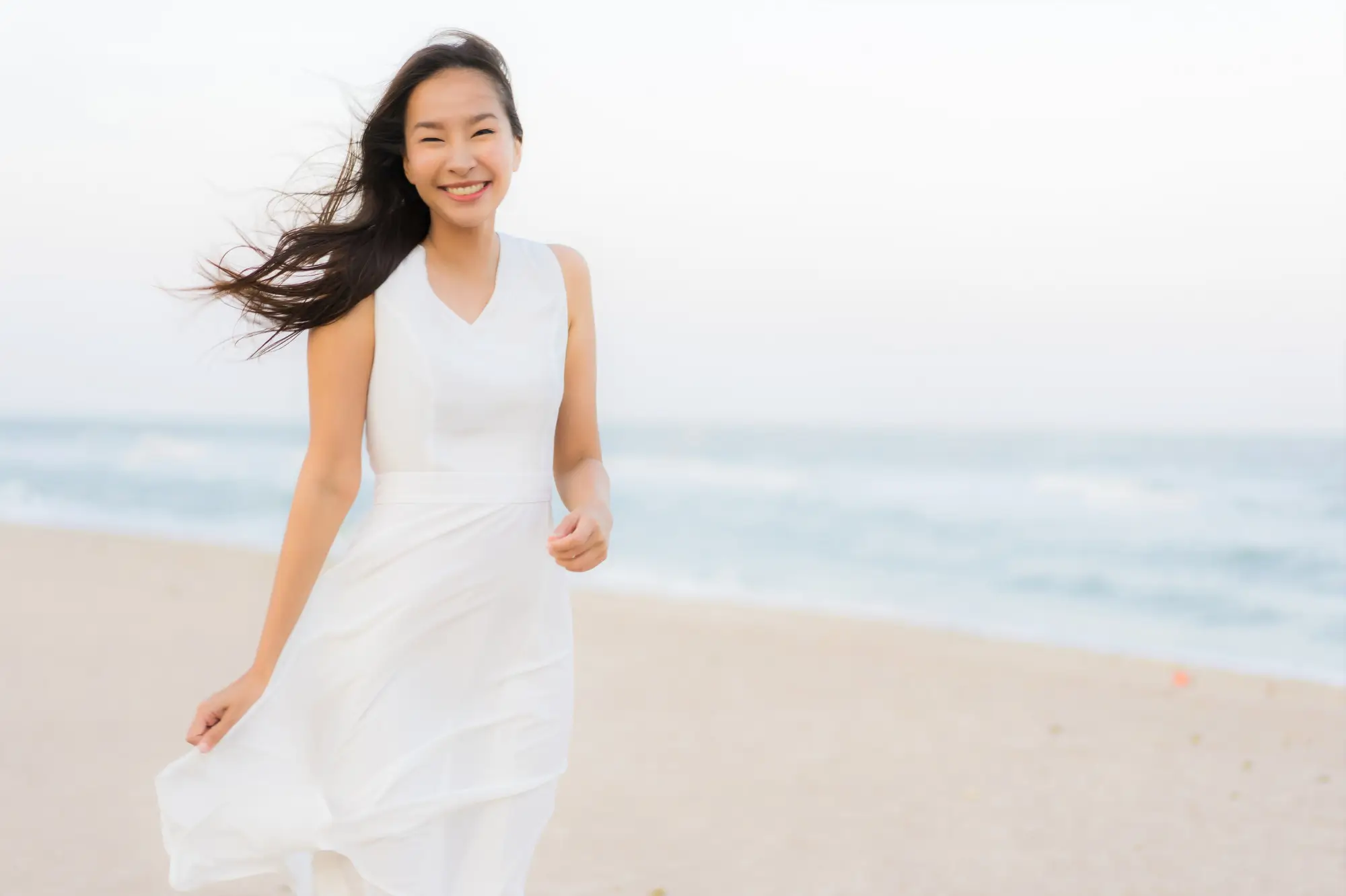 a woman stands besides beach and has a smile