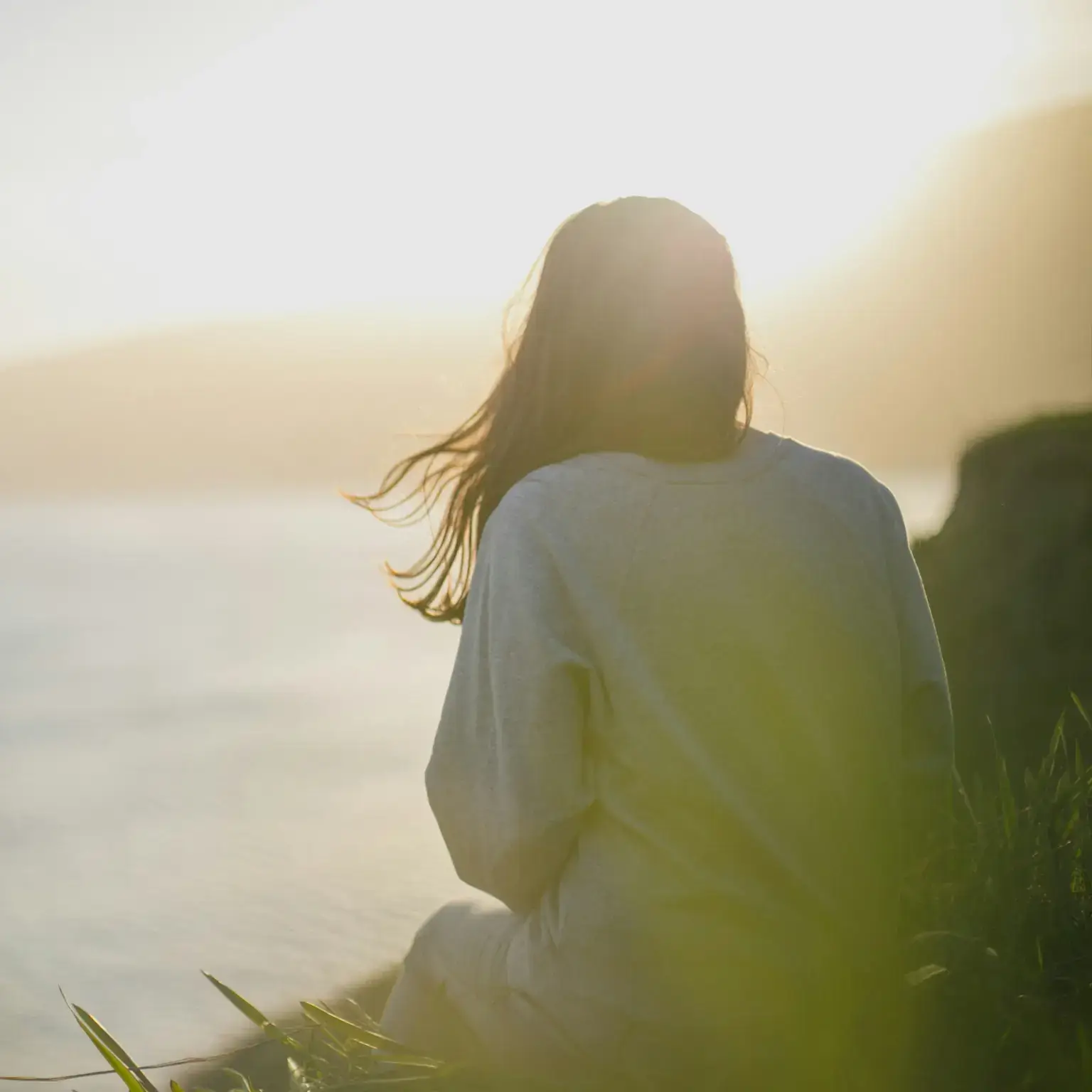 a woman sits on the grass and looking at the sunset